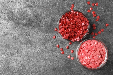 Bright heart shaped sprinkles in bowls on grey table, flat lay. Space for text