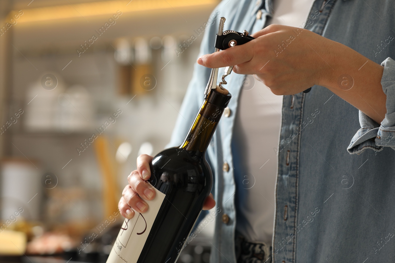 Photo of Woman opening wine bottle with corkscrew indoors, closeup. Space for text