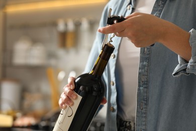 Photo of Woman opening wine bottle with corkscrew indoors, closeup. Space for text