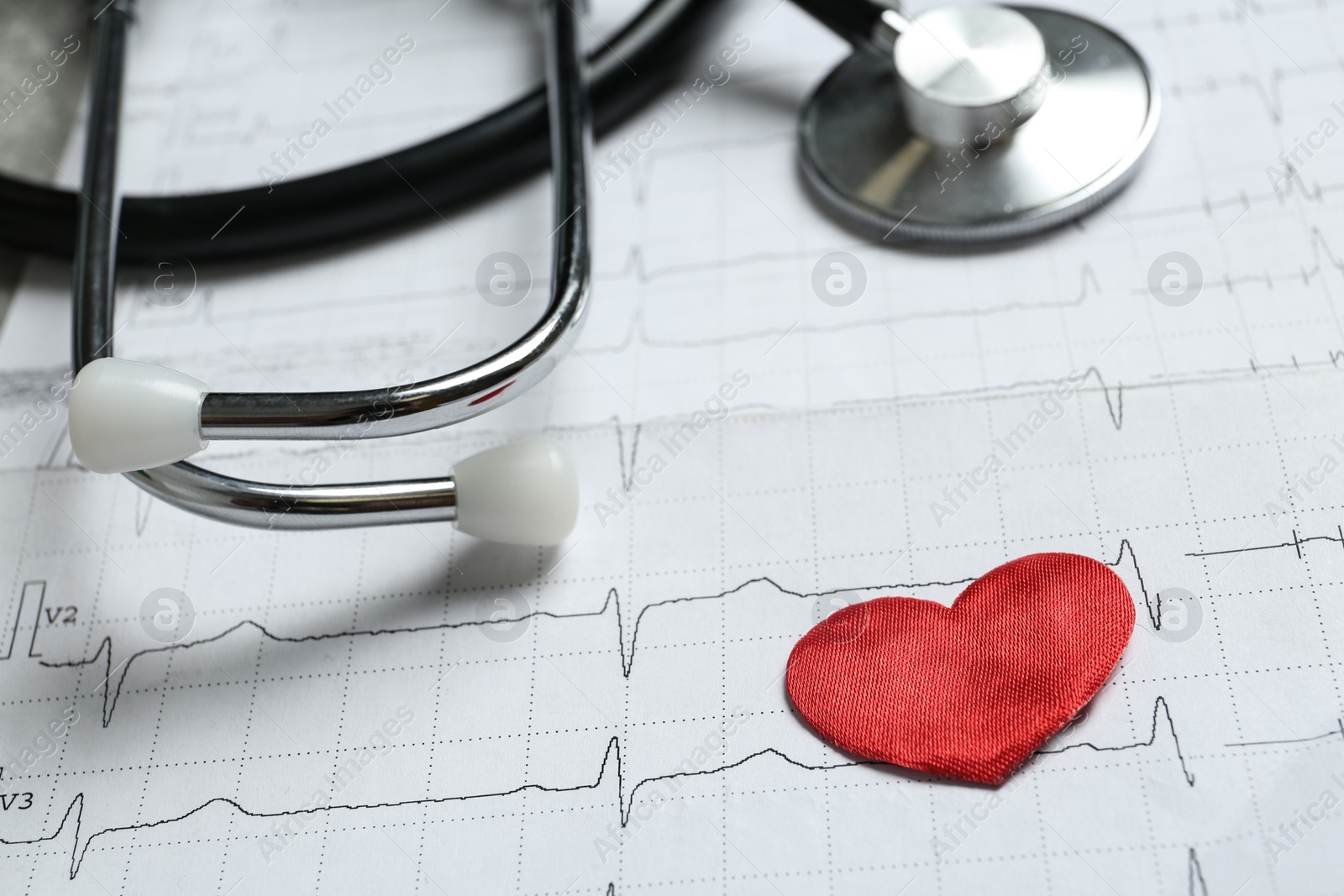 Photo of Red decorative heart and stethoscope on cardiogram report, closeup