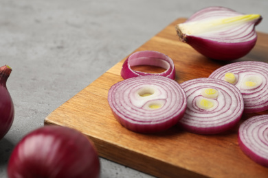 Photo of Cut red onion and wooden board on light grey table, closeup