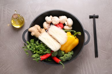 Photo of Wok, chopsticks and different products on grey textured table, flat lay