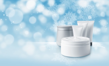 Image of Different cosmetic products on light blue background with blurred snowflakes, space for text. Winter skin care