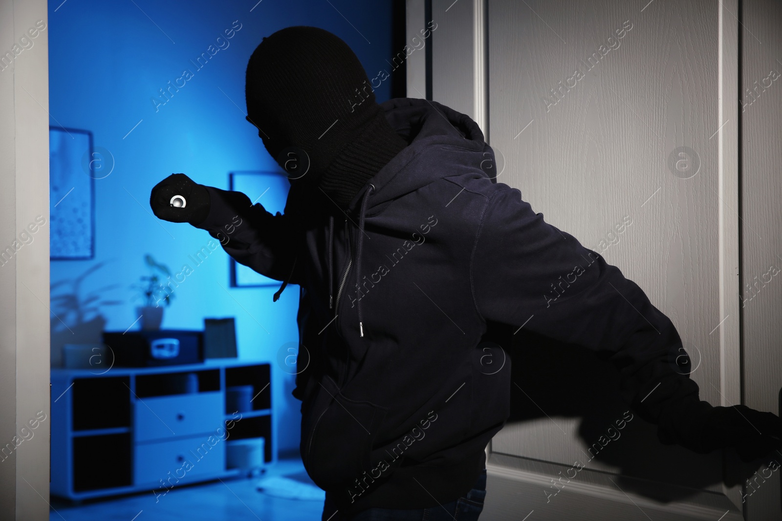 Photo of Thief with flashlight breaking into house at night