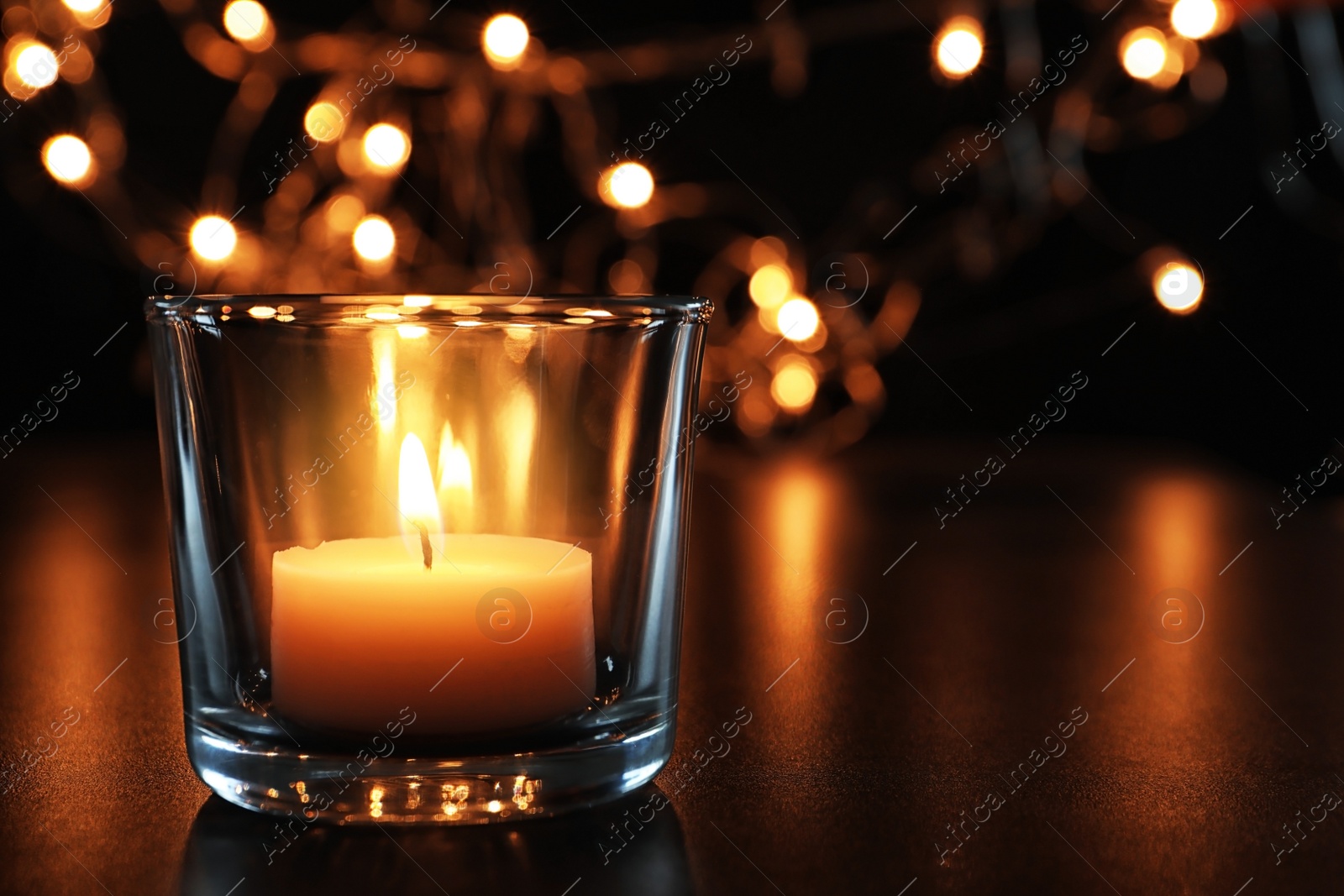 Photo of Wax candle burning on table in darkness, closeup