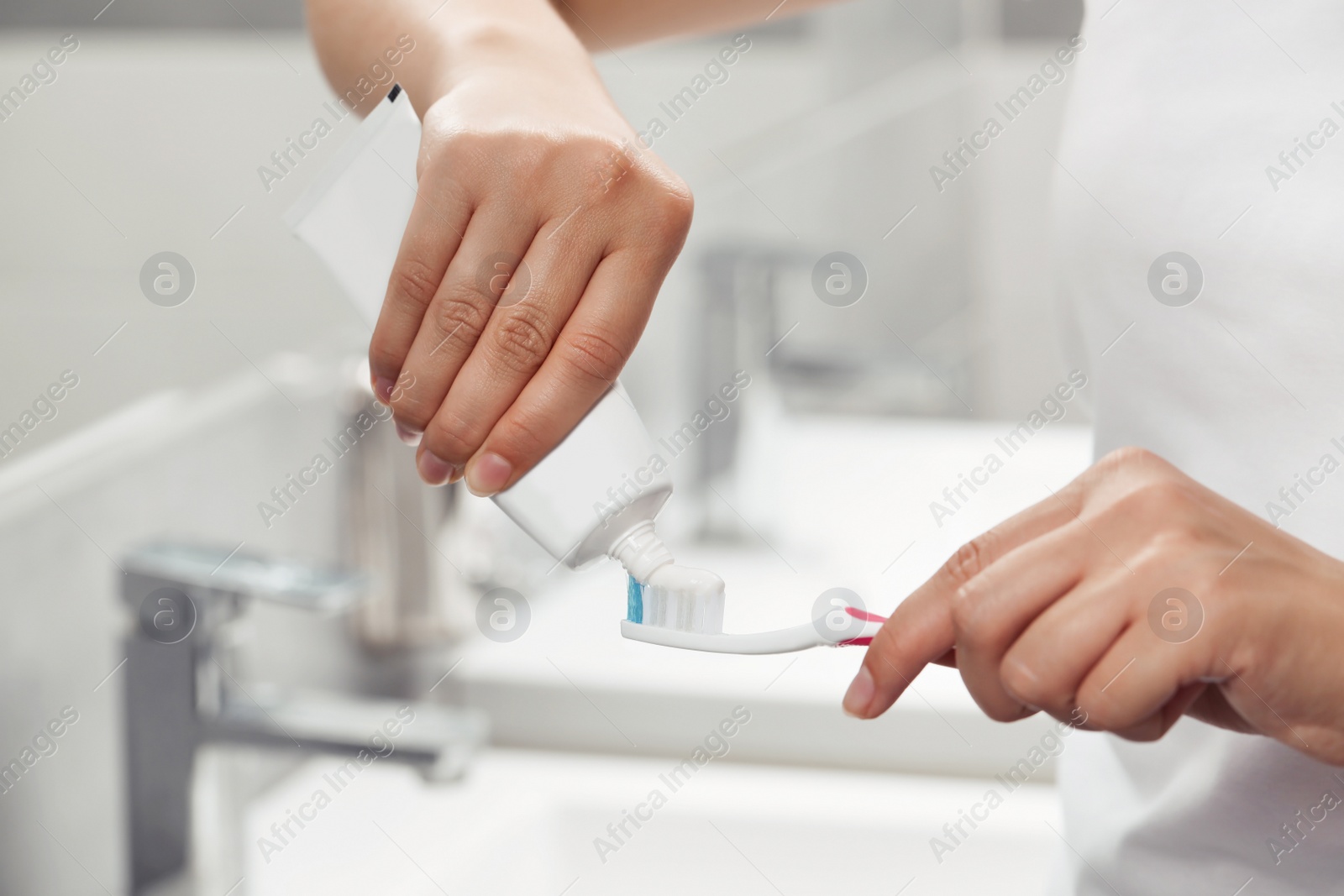 Photo of Woman applying toothpaste on brush in bathroom, closeup