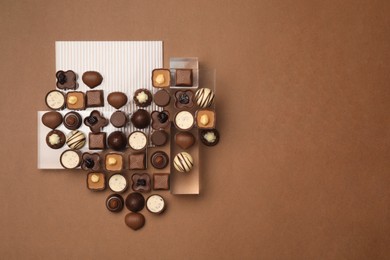 Photo of Heart made with delicious chocolate candies on brown background, top view. Space for text