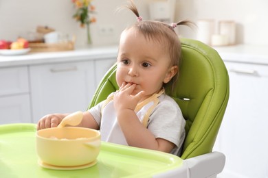 Photo of Cute little baby eating food in high chair at kitchen