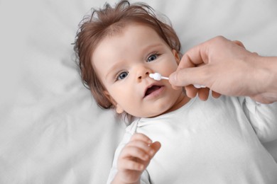 Photo of Father cleaning nose of his baby with cotton bud on bed, top view
