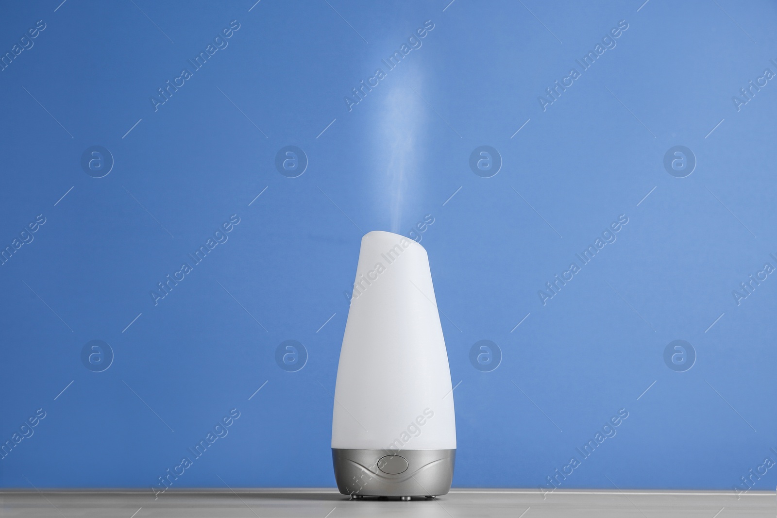 Photo of Modern essential oil diffuser on wooden table against blue background