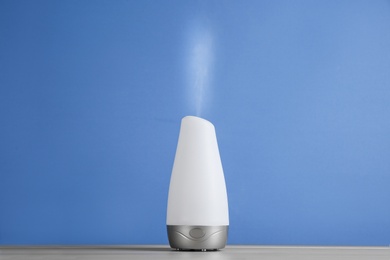 Modern essential oil diffuser on wooden table against blue background