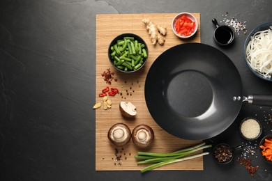 Flat lay composition with black wok, spices and products on dark textured table. Space for text