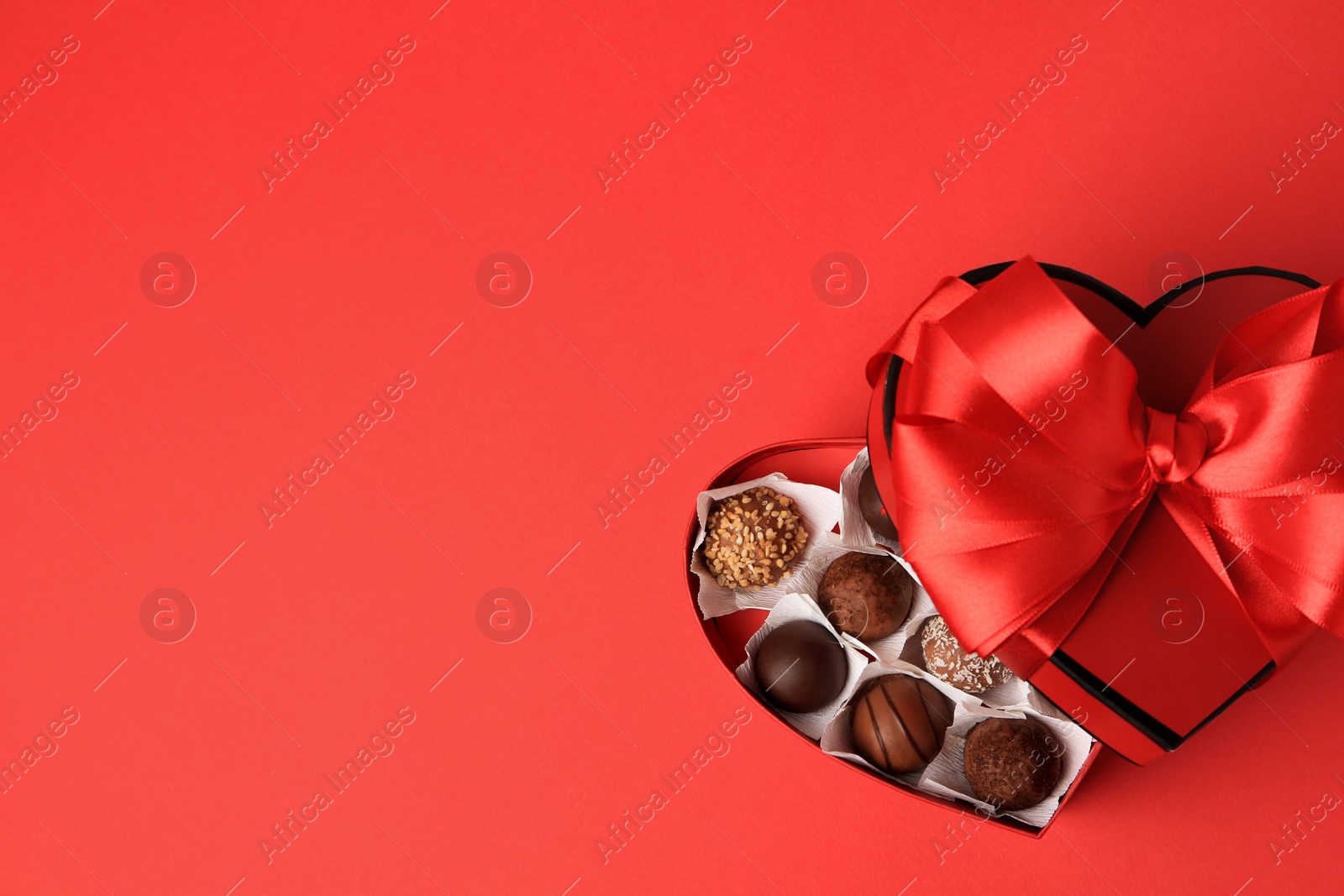 Photo of Heart shaped box with delicious chocolate candies on red table, top view. Space for text