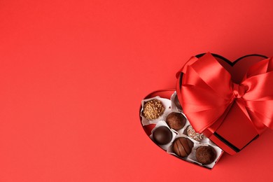 Heart shaped box with delicious chocolate candies on red table, top view. Space for text