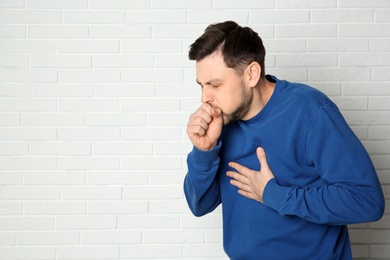 Man suffering from cough near brick wall. Space for text