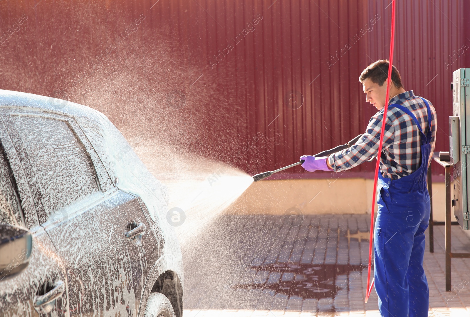 Photo of Worker cleaning automobile with high pressure water jet at car wash