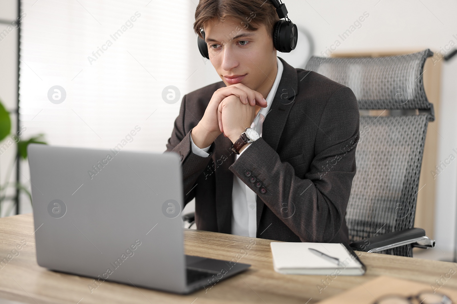 Photo of Man in headphones watching webinar at wooden table in office