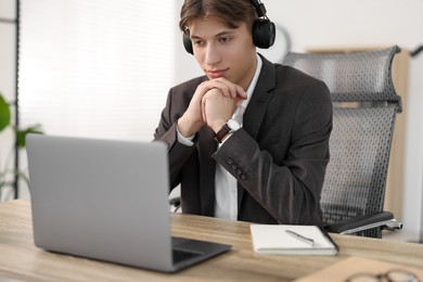 Photo of Man in headphones watching webinar at wooden table in office