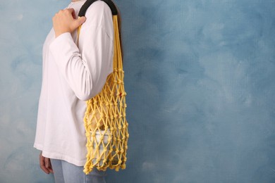 Photo of Woman with net bag full of different items near light blue wall, closeup and space for text. Conscious consumption