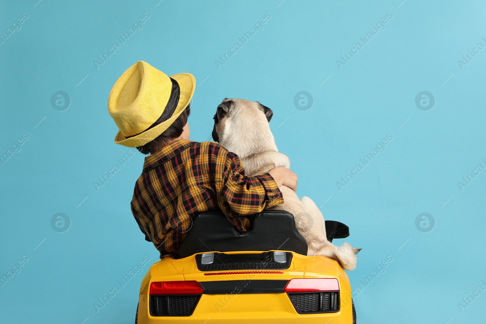 Photo of Little boy with his dog in toy car on light blue background, back view