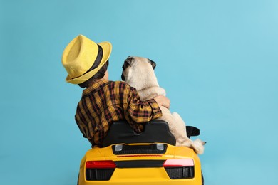 Little boy with his dog in toy car on light blue background, back view