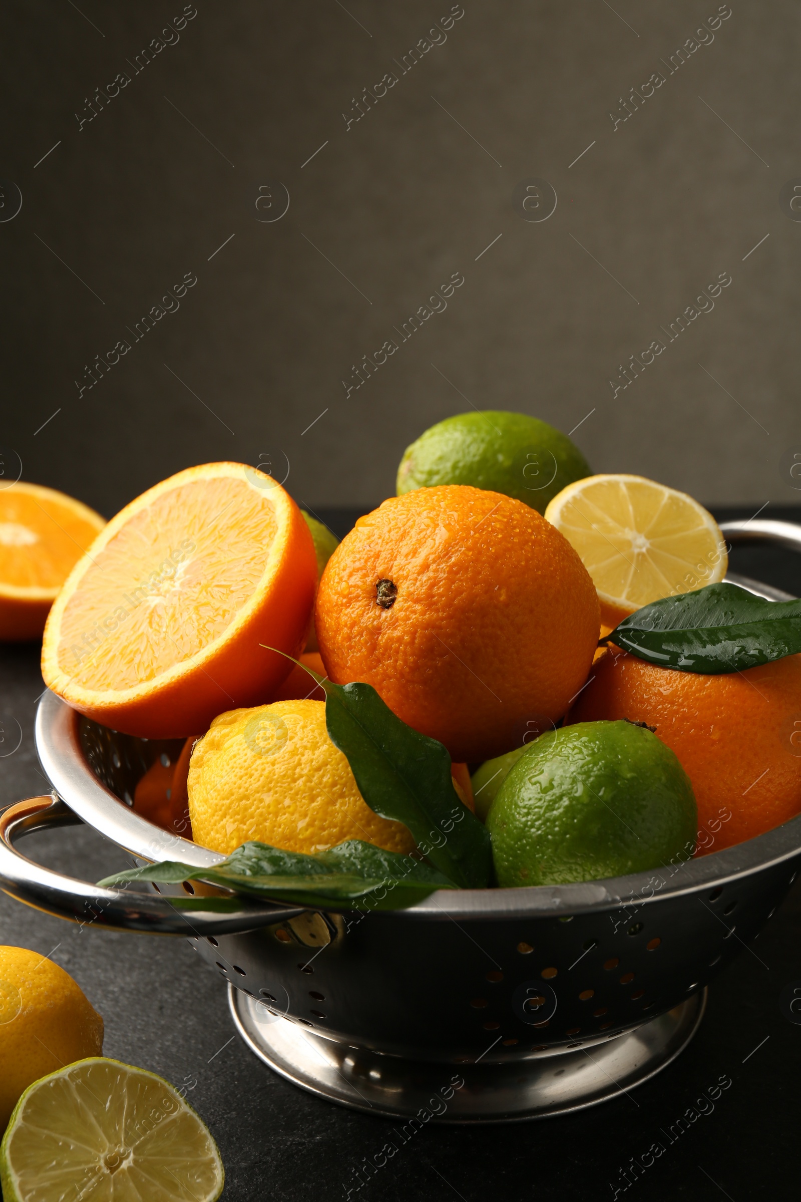 Photo of Fresh citrus fruits in colander on dark table, closeup