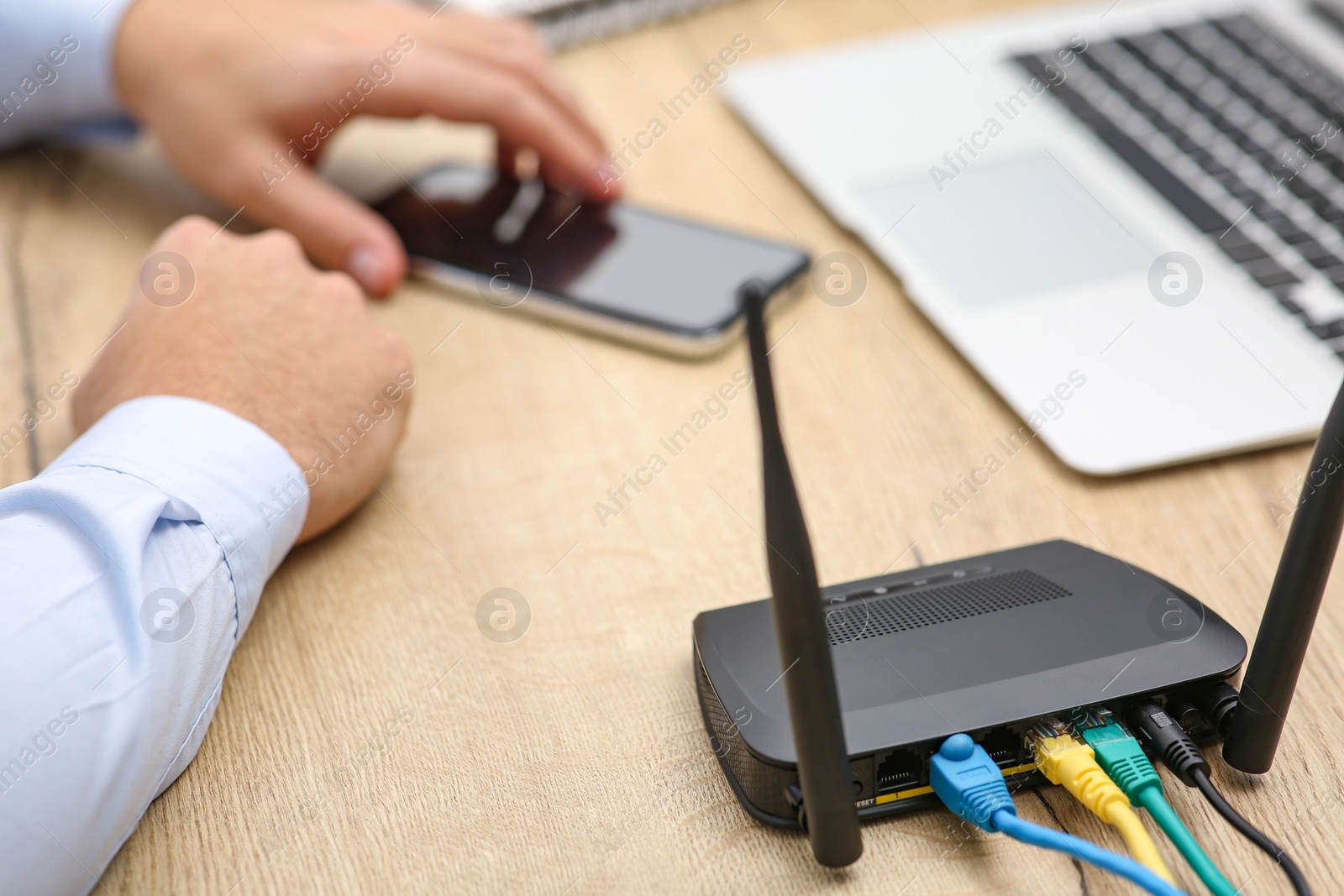 Photo of Man with laptop and smartphone connecting to internet via Wi-Fi router at wooden table indoors, closeup