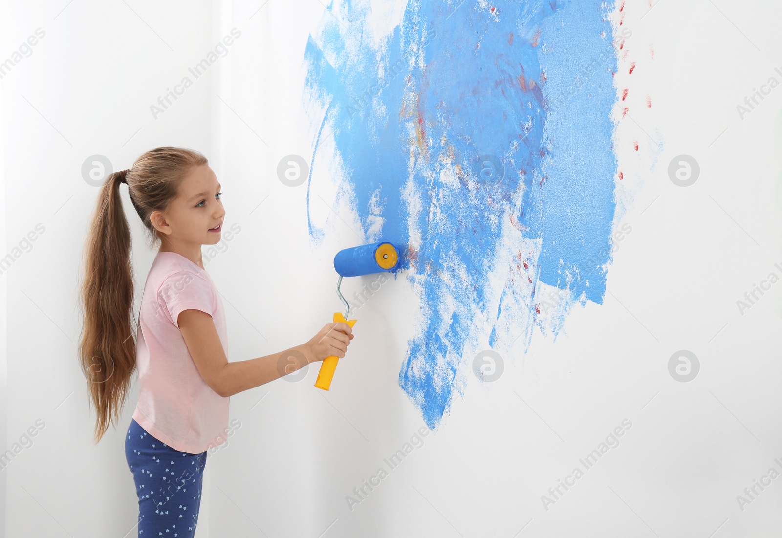 Photo of Little child painting wall with roller brush indoors