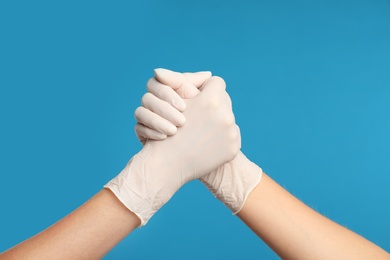 Doctors in medical gloves shaking hands on light blue background, closeup