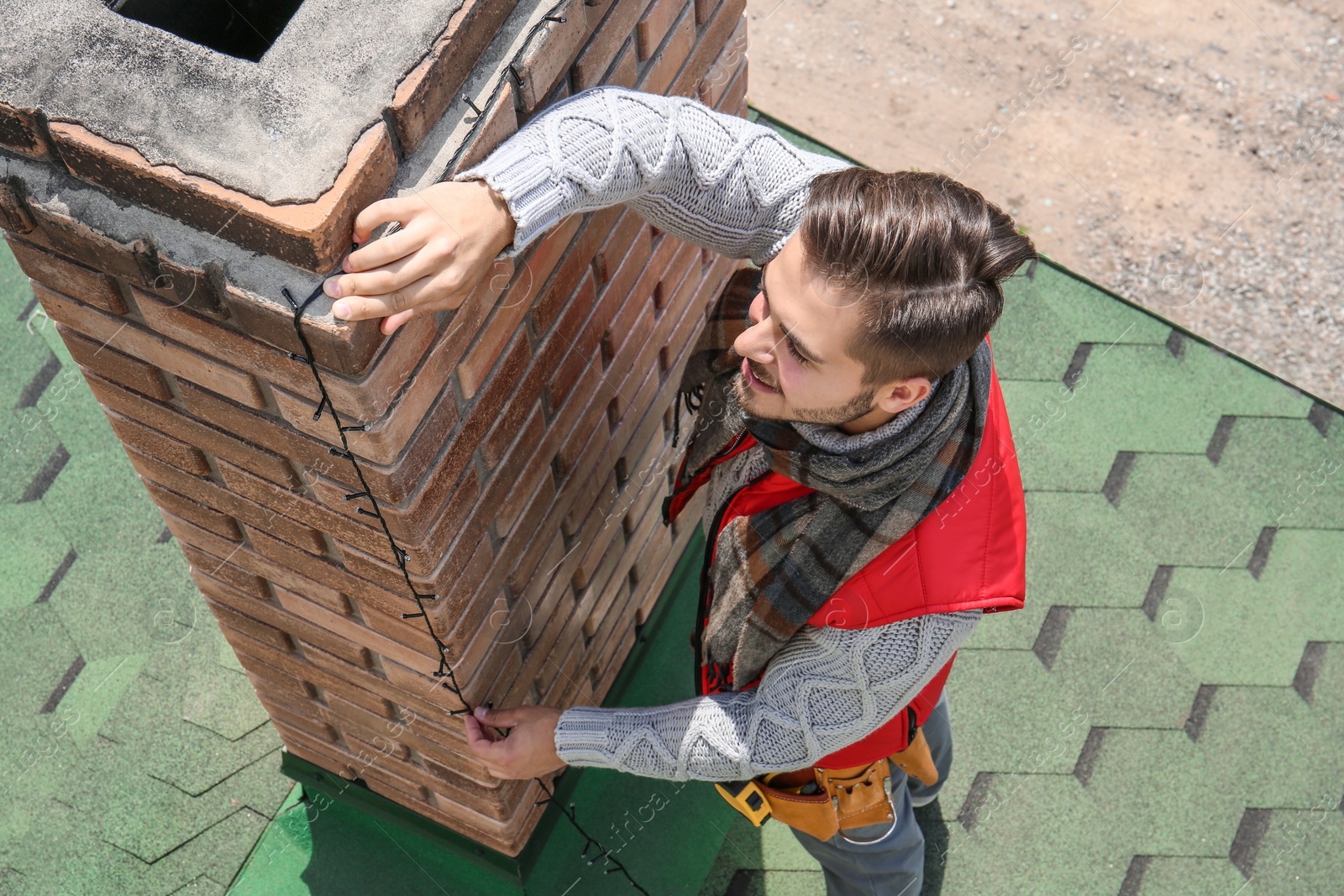 Photo of Young man decorating chimney with Christmas lights