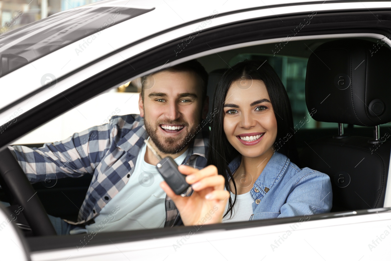 Photo of Happy couple with car key sitting in modern auto at dealership