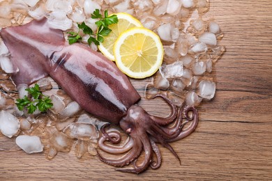 Photo of Fresh raw squid with ice, lemon and parsley on wooden table, flat lay