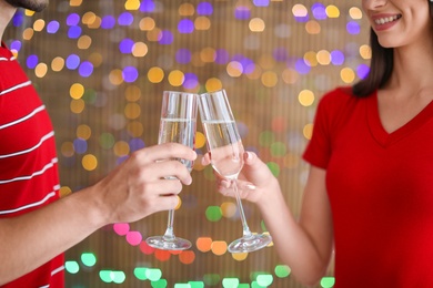 Photo of Young couple clinking glasses of champagne on blurred lights background. Christmas celebration