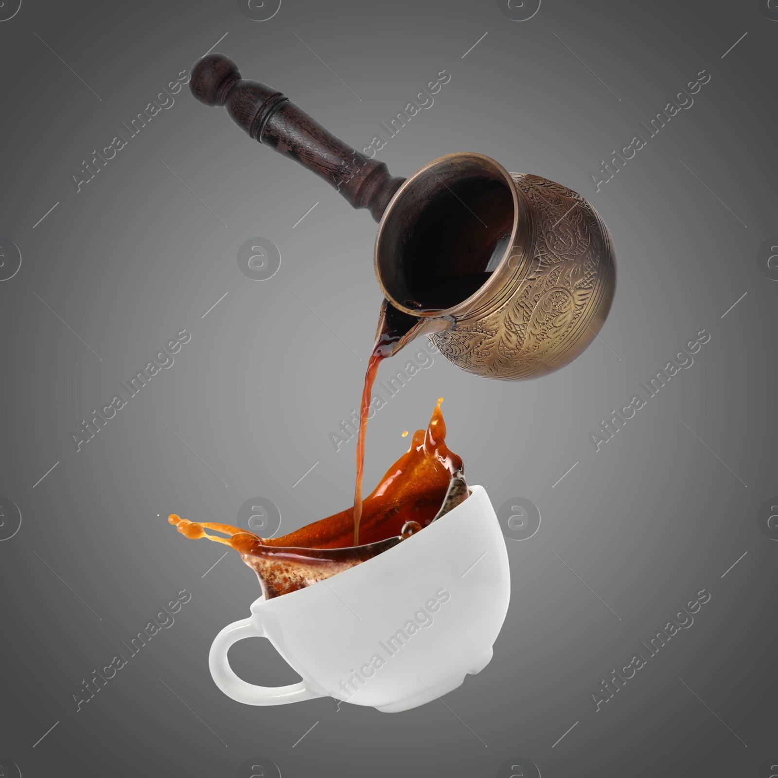 Image of Pouring freshly brewed aromatic coffee from turkish pot into cup. Objects in air on grey background