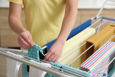 Photo of Young woman hanging clean laundry on drying rack in bathroom, closeup