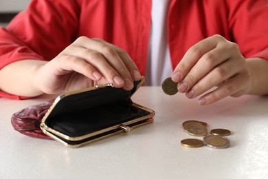 Photo of Poor woman putting coin into empty wallet at white table, closeup