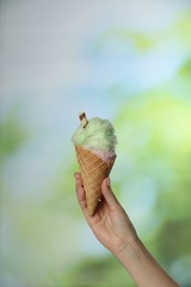 Photo of Woman holding waffle cone with cotton candy on blurred background, closeup