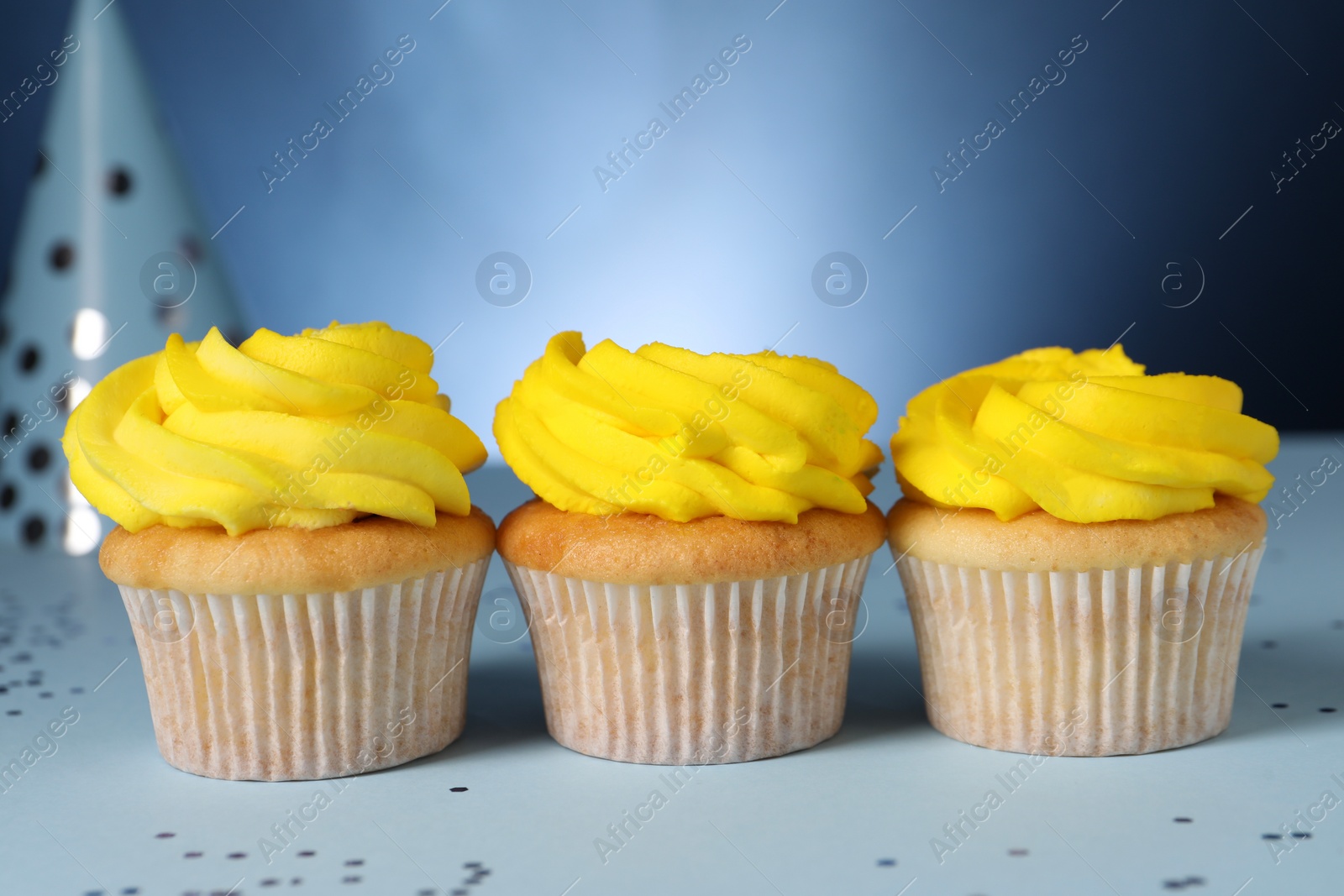 Photo of Delicious cupcakes with bright cream and confetti on blue background