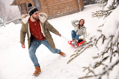 Photo of Young man pulling sled with his girlfriend outdoors on snowy day. Winter vacation