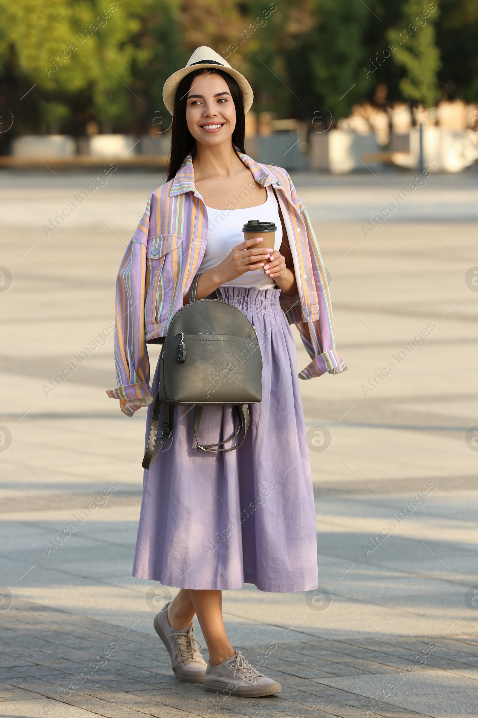 Photo of Beautiful young woman with stylish black backpack and coffee on city street