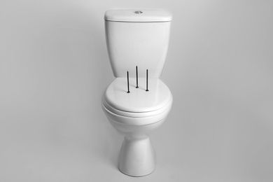 Photo of Toilet bowl with nails on white background. Hemorrhoids concept