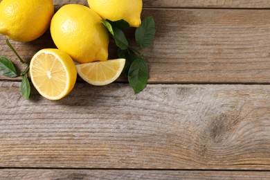 Photo of Fresh lemons and green leaves on wooden table, flat lay. Space for text