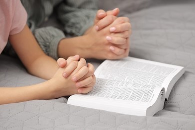 Photo of Girl and her godparent praying over Bible together indoors, closeup
