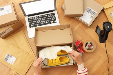 Photo of Woman packing sneakers into cardboard box at wooden table, top view. Online store