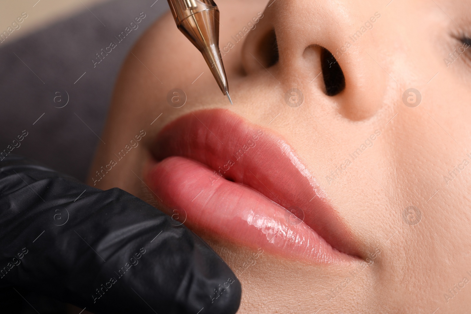 Photo of Young woman undergoing procedure of permanent lip makeup in tattoo salon, closeup