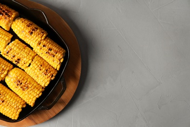 Photo of Fresh grilled tasty corn cobs in pan and space for text on light background, top view