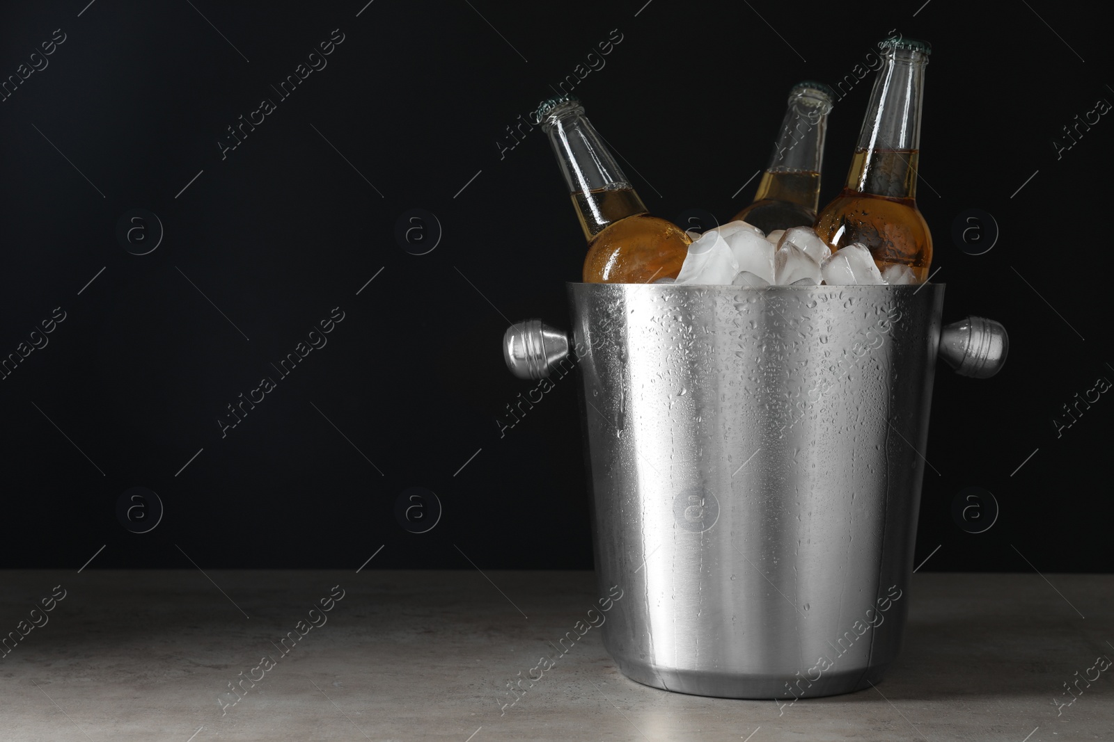 Photo of Metal bucket with bottles of beer and ice cubes on grey table. Space for text