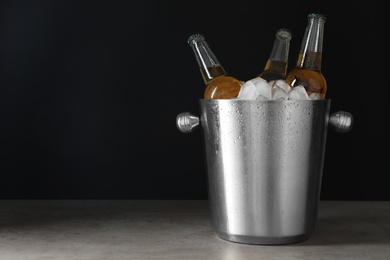 Photo of Metal bucket with bottles of beer and ice cubes on grey table. Space for text