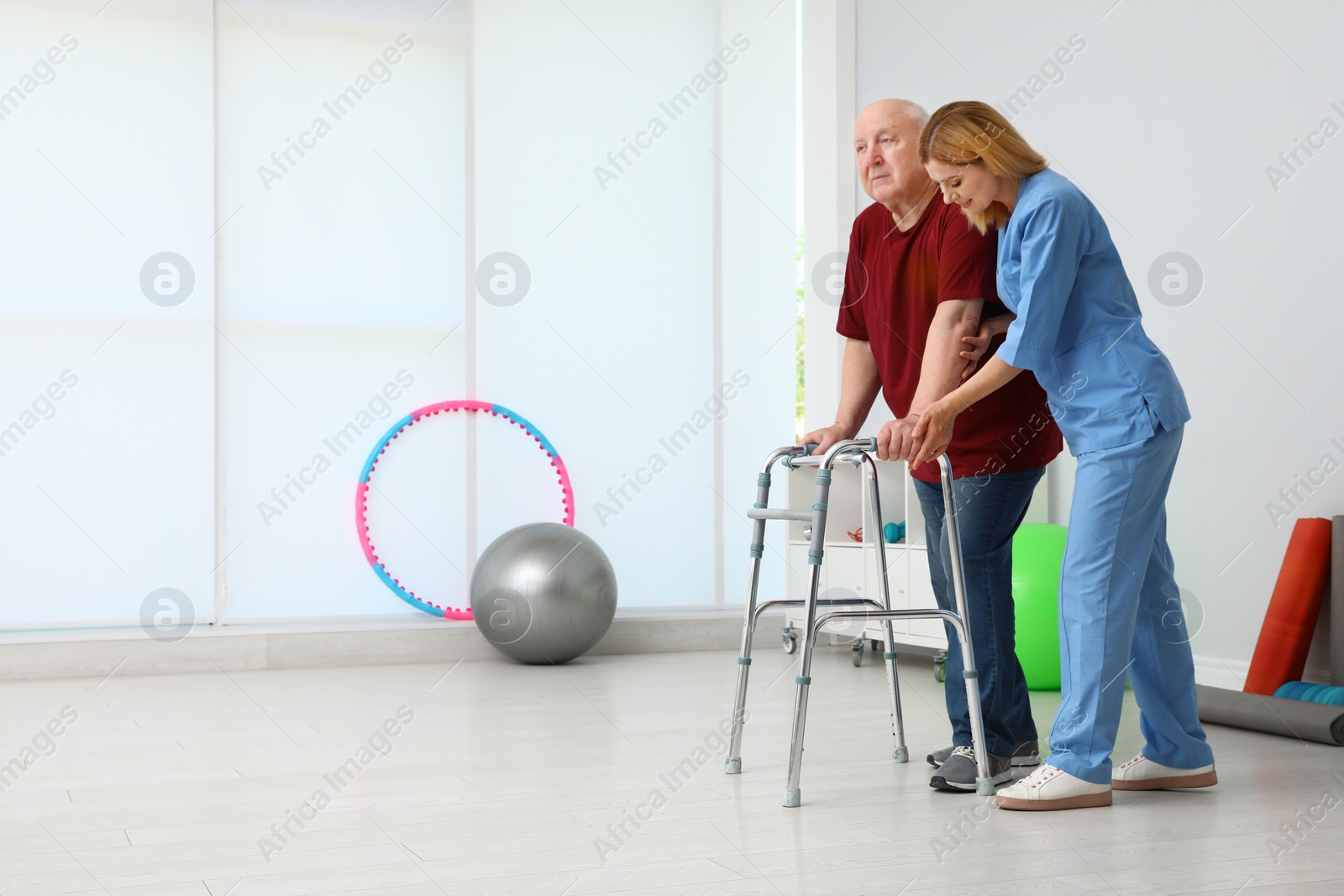 Photo of Caretaker helping elderly man with walking frame indoors