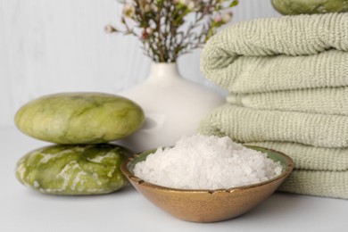 Photo of Composition with sea salt, spa stones, towels and flowers on white table against wooden background, closeup